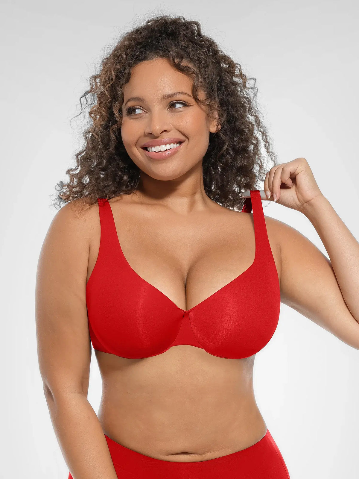 Model adjusting the wide no-dig shoulder straps on a bright red unlined underwire bra for custom pressure relief
