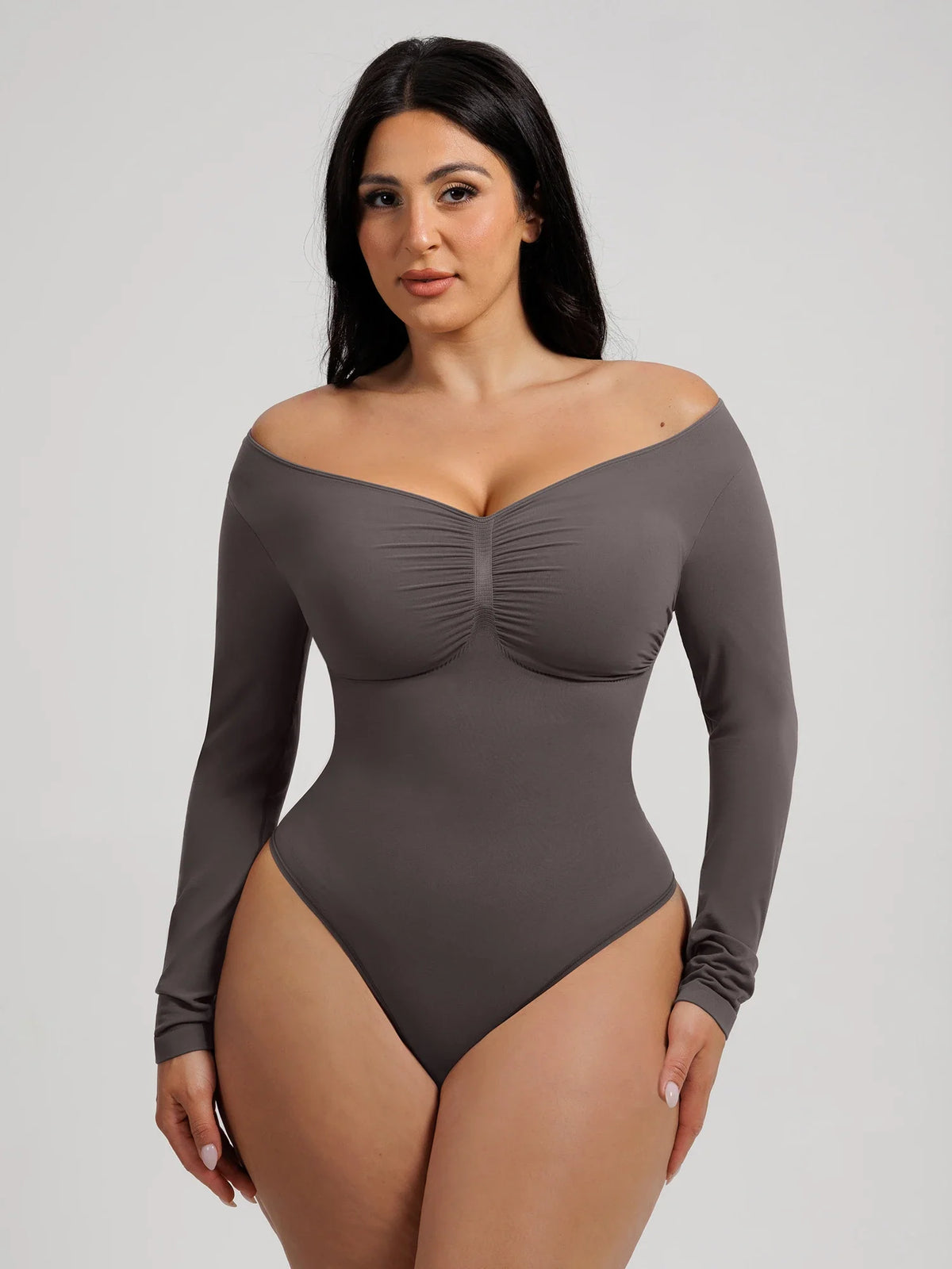Model styling a slate gray long-sleeve bodysuit with an off-the-shoulder neckline highlighting the collarbones